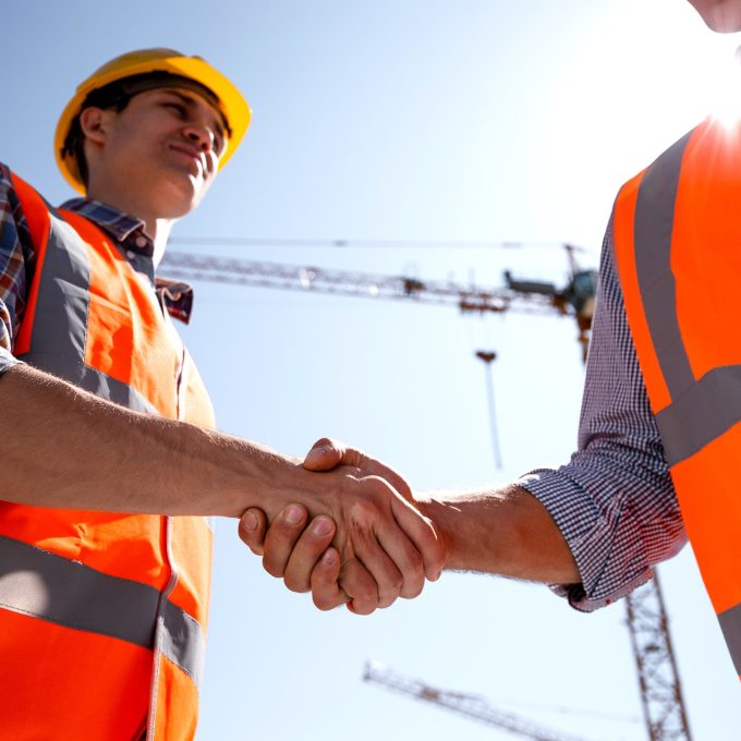 structural-engineer-and-architect-dressed-in-orange-work-vests-and-helmets-shake-hands-on-the.jpg